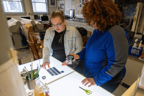 Image of two students viewing photography negatives on an illuminated light table.