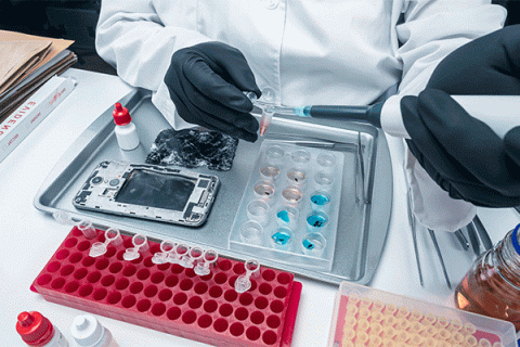 Detail photo a person working in a lab with a white lab coat and gloves working on a phone damaged by fire. 